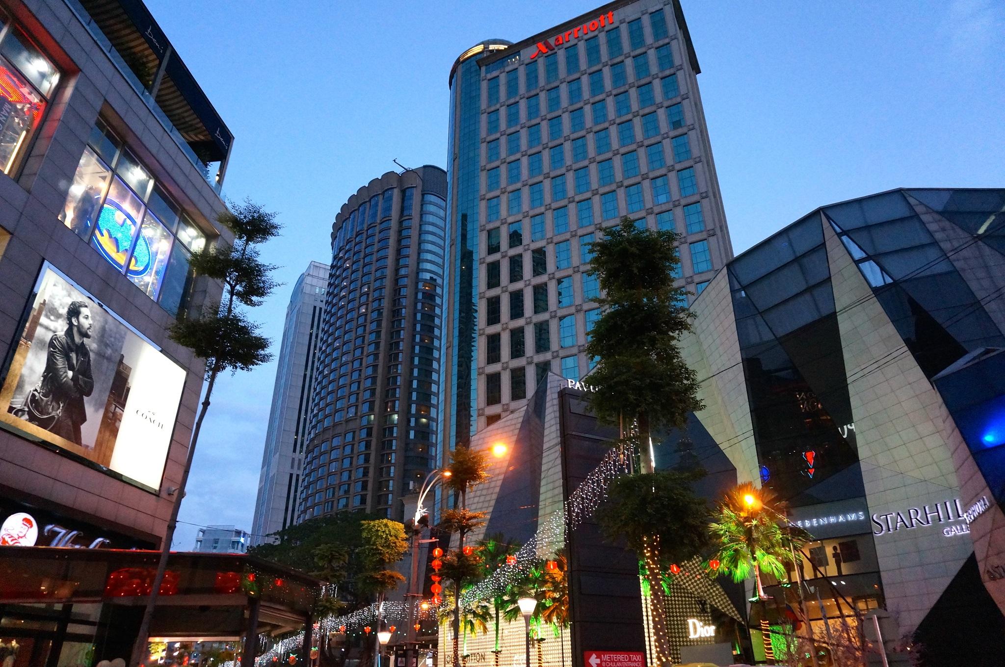 מלון Jw Marriott קואלה לומפור מראה חיצוני תמונה The photo shows a modern urban scene during twilight. There are several tall buildings, including a notable high-rise with a glass facade, suggesting a commercial area. The architecture appears contemporary, with a mix of reflective surfaces and illu