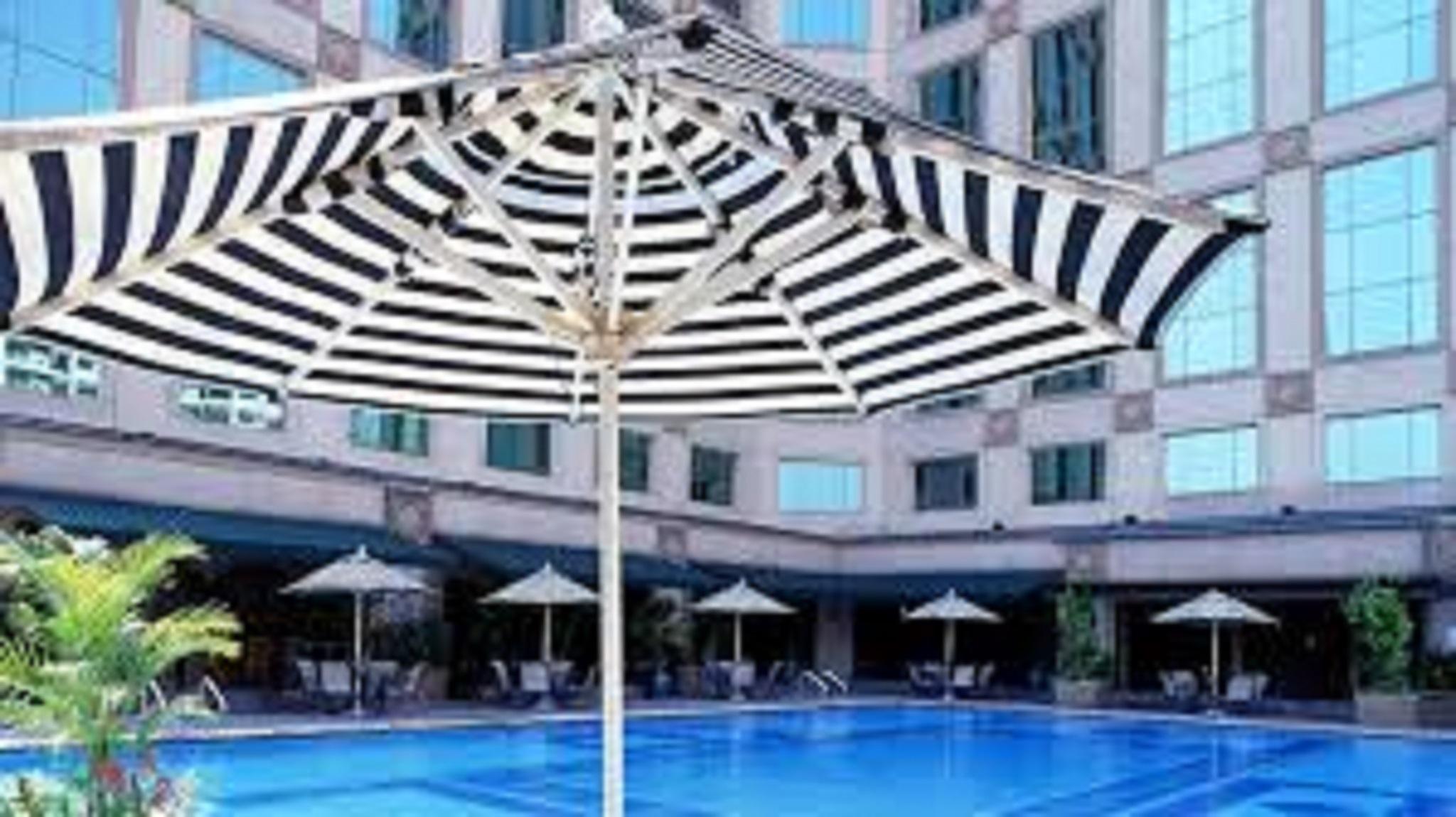 מלון Jw Marriott קואלה לומפור מראה חיצוני תמונה The photo shows a swimming pool surrounded by a deck and several striped umbrellas providing shade. The pool has a clear blue water surface, and there are seating areas with lounges or chairs visible near the pool. The surrounding buildings have larg