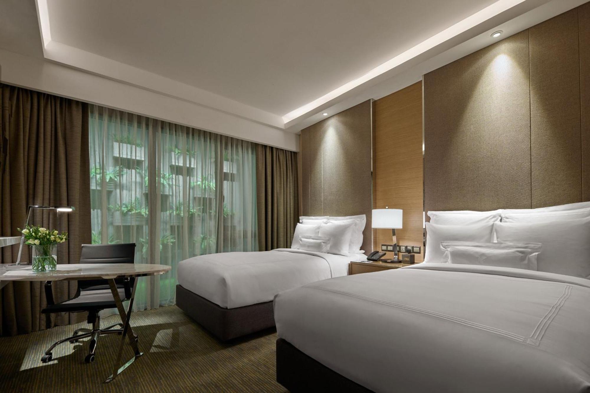 מלון Jw Marriott קואלה לומפור מראה חיצוני תמונה The photo shows a modern hotel room featuring two beds with white bedding. The walls are styled with a combination of textured panels and soft lighting. There's a large window draped with sheer curtains, allowing natural light to enter the room. A sm