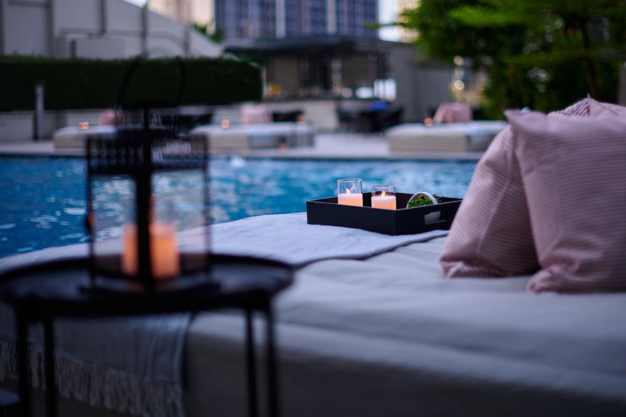 מלון Jw Marriott קואלה לומפור מראה חיצוני תמונה The photo depicts a serene setting by a pool. In the foreground, there is a table with a lantern and candles, creating a cozy atmosphere. A tray on a lounge area holds three glasses and some greenery. Soft pillows add comfort, and the pool reflects t