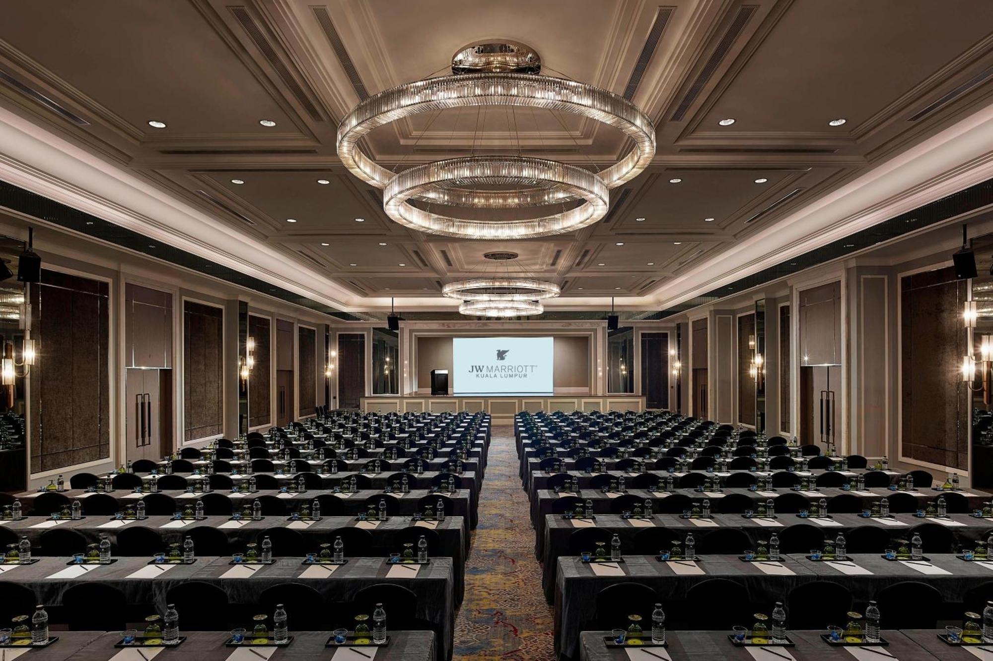 מלון Jw Marriott קואלה לומפור מראה חיצוני תמונה The photo shows a large conference room set up for a meeting or event. There are numerous rows of tables arranged in a classroom or theater style, with chairs facing the front where a large screen is set up, likely for presentations. The room has ele